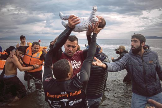 SEORANG sukarelawan membawa seorang bayi turun dari bot manakala rakan-rakannya membantu pelarian dan pendatang lain ke darat selepas tiba di pulau Lesbos, Greece, dari Turki.