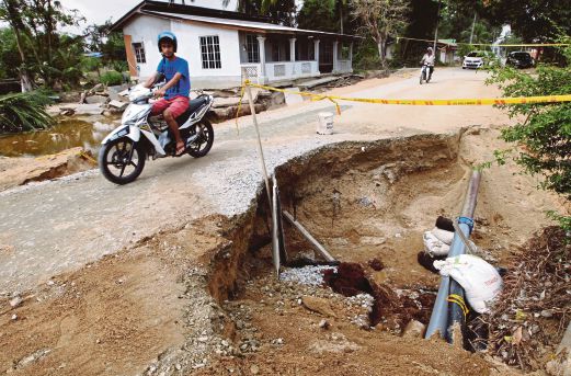  Penduduk menggunakan jalan terhakis      yang membentuk lubang sedalam empat meter di Kampung  Tok Sadang,  Kedai Buloh, semalam. 