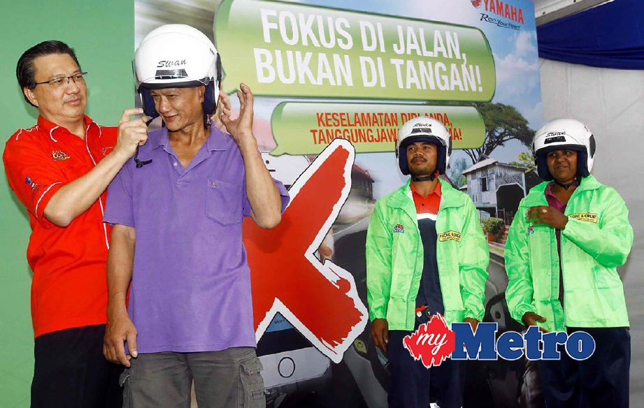 Tiong Lai memakaikan topi keledar kepada salah seorang pengguna motosikal yang menyertai kempen. FOTO Muhd Asyraf Sawal