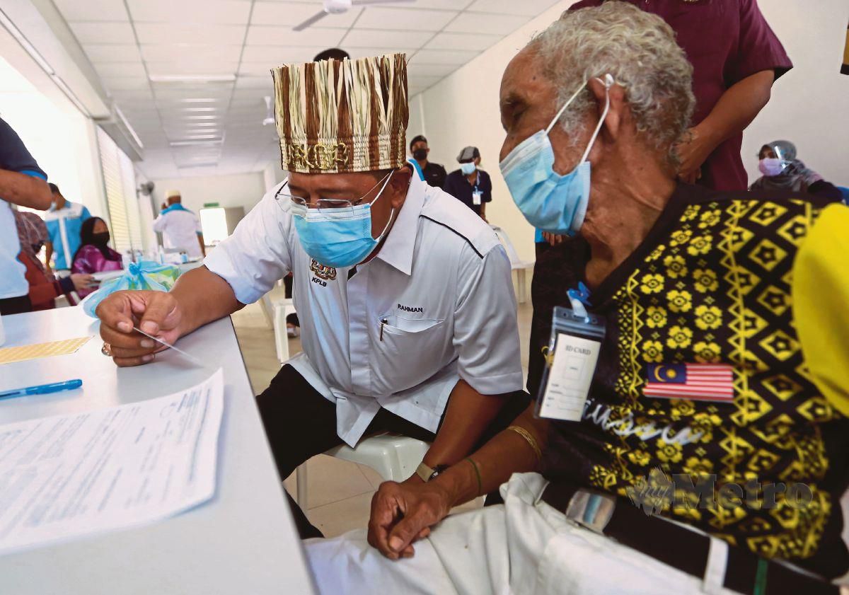 ABDUL Rahman (kiri) melihat kad pengenalan warga emas, Long Senah, 88, pada Program Vaksinasi Masyarakat Orang Asli di OAOSC, Kampung Bawong, Sungai Siput. FOTO SHARUL HAFIZ ZAM
