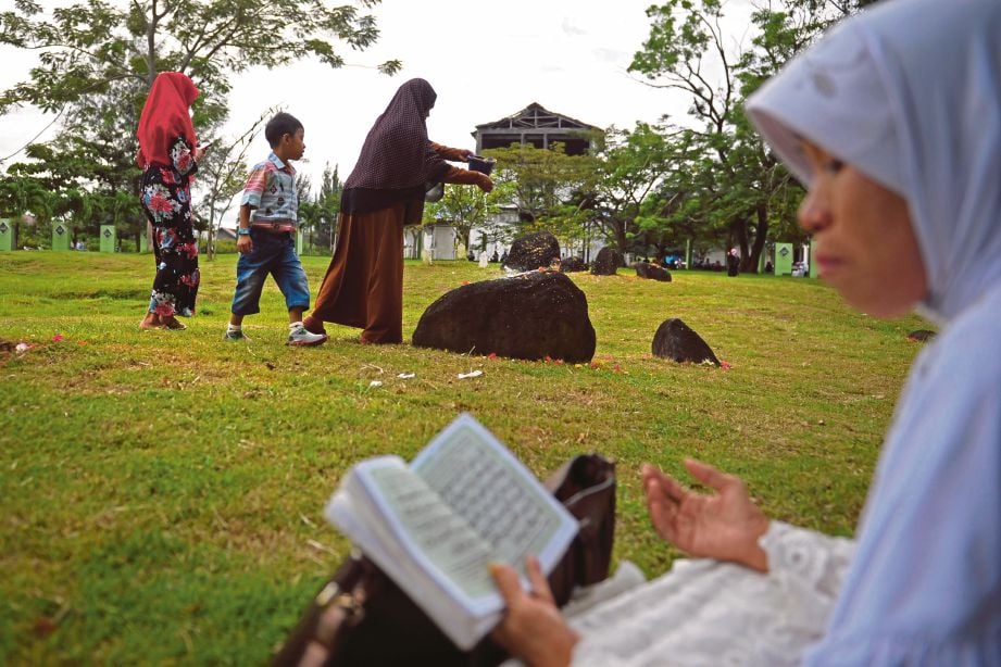 SEORANG wanita membaca al-Quran di kawasan perkuburan yang menempatkan mangsa tsunami di Aceh semalam. - AFP 
