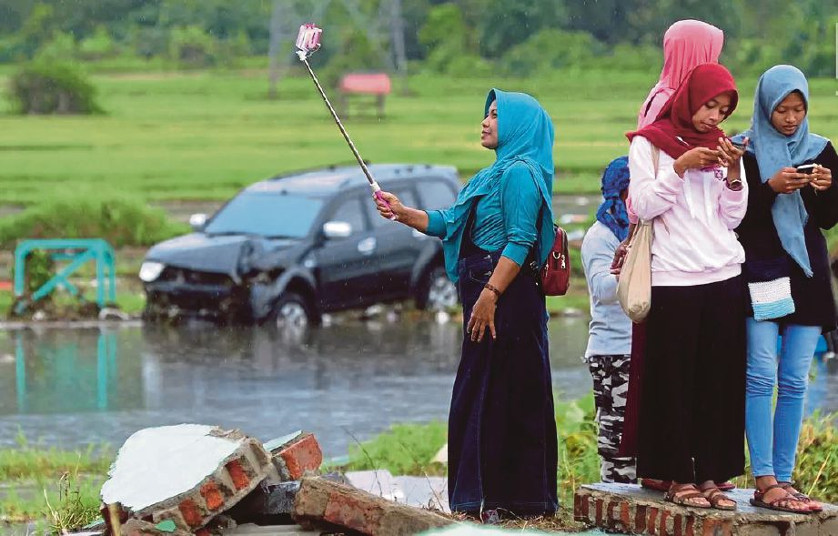 SEORANG wanita merakam  swafoto di kawasan bencana di Banten. - Merdeka.com