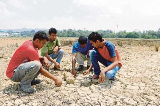 MOHD Zulkifli (kanan) bersama rakannya memeriksa keadaan tanah sawah yang merekah di Kampung Pangkal Chuit, Machang. 