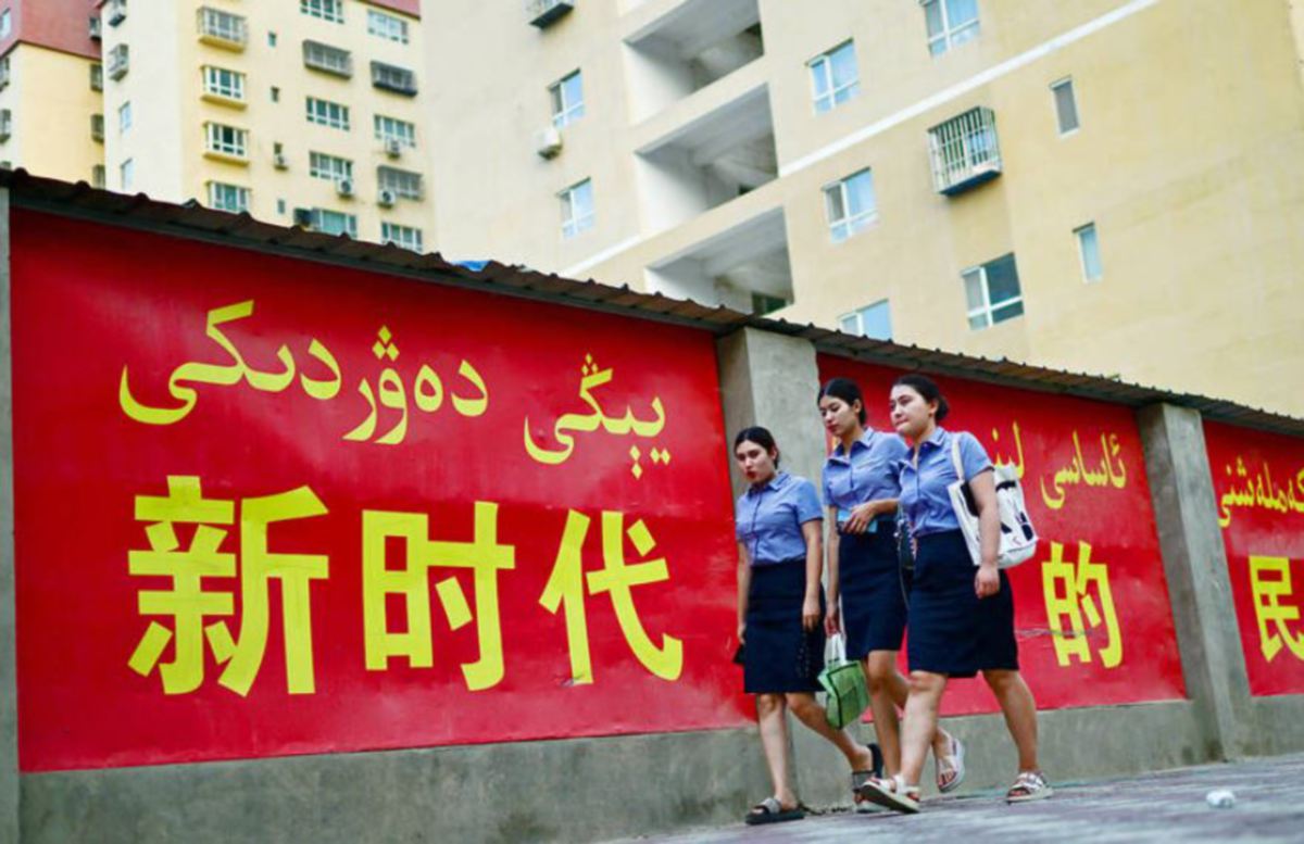 WANITA berjalan di tepi slogan propaganda yang mempromosikan perpaduan etnik di Yarkant wilayah Xinjiang, China. FOTO AFP.
