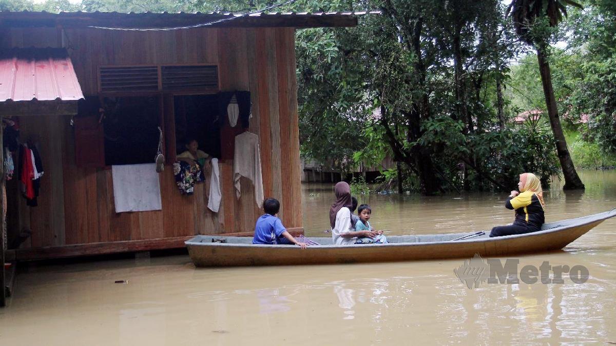 WAN Rohani Wan Salleh, 44, bersama anaknya menaiki perahu untuk pergi rumah ke rumah, semalam selepas kediaman mereka i Kampung Tersang, Rantau Panjamg dinaiki air. FOTO Nik Abdullah Nik Omar