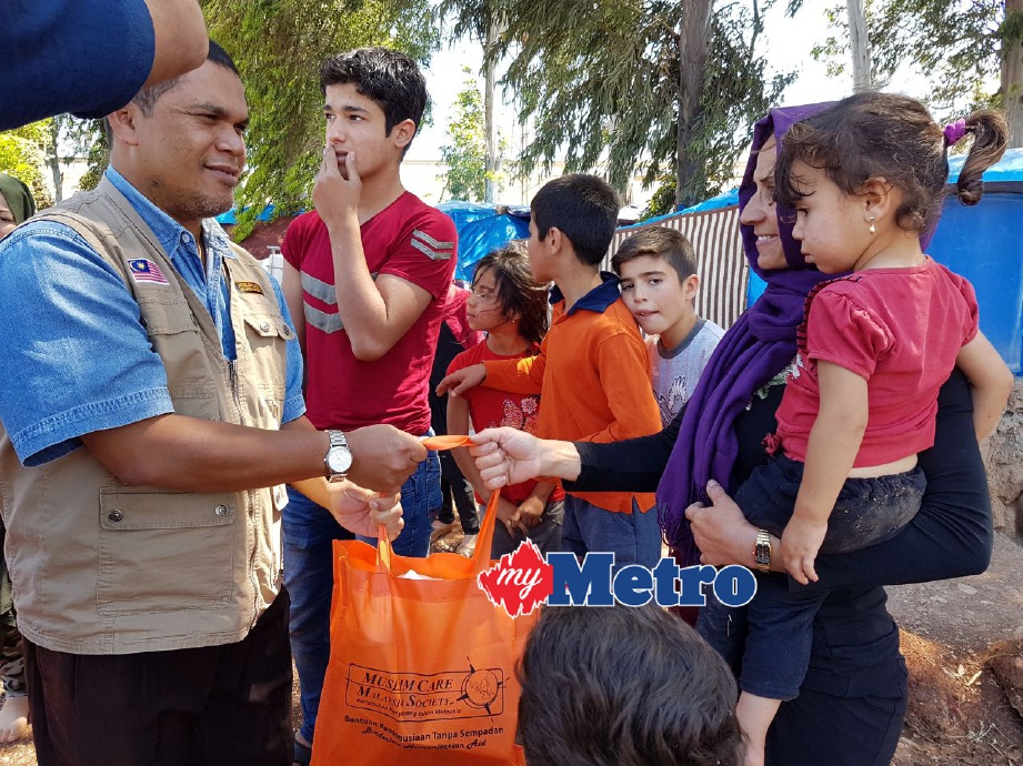 Zulkifli (kiri) menyerahkan bantuan keperluan makanan asas kepada pelarian Syria yang tinggal di khemah pinggir bandar Reyhanli. FOTO Amir Abd Hamid