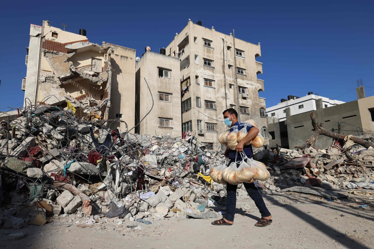 PENJUAL roti melalui runtuhan bangunan yang musnah akibat serangan rejim zionis di Semenanjung Gaza. FOTO AFP 