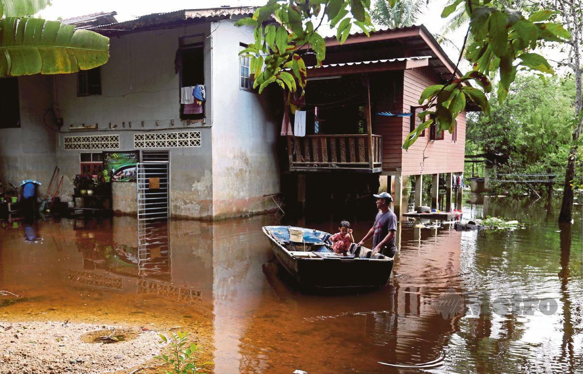 MOHD Irwan menggunakan sampan untuk meninjau keadaan sekitar rumah yang ditenggelami banjir  di Kampung Tersang, Rantau Panjang. FOTO NIK ABDULLAH NIK OMAR