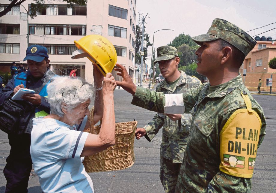 SEORANG askar membantu seorang wanita warga emas memakai topi keledar sebelum dibenarkan masuk ke apartmen miliknya untuk mengambil barangan peribadi. - AFP 