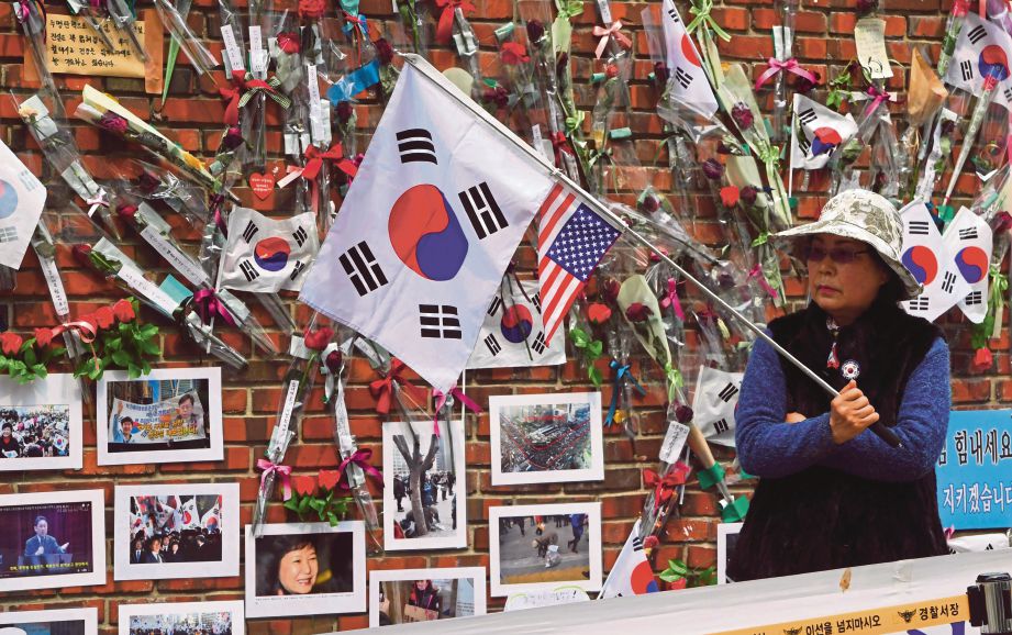 PENYOKONG bekas Presiden Park berdiri di hadapan tembok yang dihiasi bunga ros dan gambar  Park di luar kediaman bekas pemimpin itu di Seoul, semalam. - AFP 