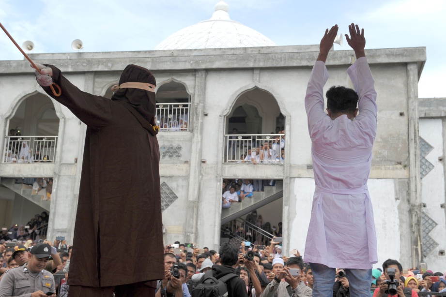 SEORANG petugas (kiri) menyebat seorang lelaki yang dihukum selepas didapati bersalah berkhalwat dengan seorang wanita di Banda Aceh, semalam. - AFP