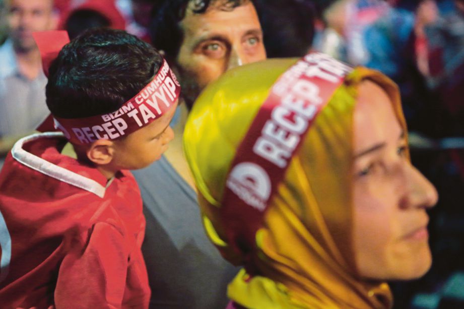 SEORANG wanita dan budak lelaki memakai lilit kepala dengan nama Presiden Recep Tayyip Erdogan ketika mengambil bahagian dalam perhimpunan menolak cubaan rampasan kuasa di Dataran Taksim, Istanbul, semalam. - AP  