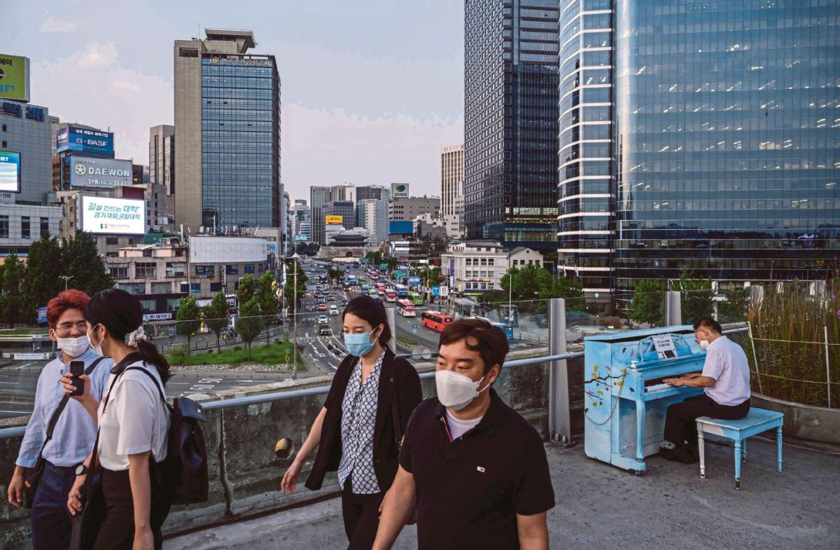 Penduduk Korea Selatan memakai pelitup muka berjalan melepasi pemain piano di Seoul. FOTO AFP.
