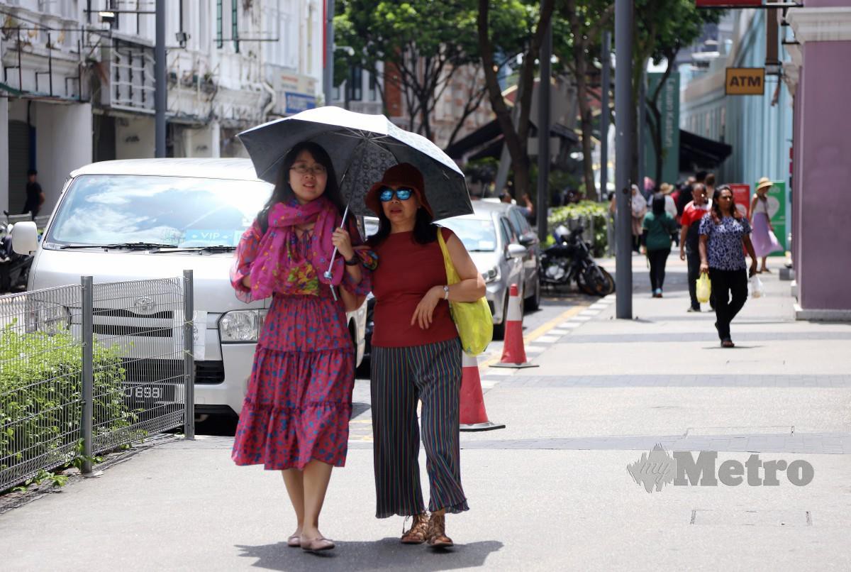 DUA wanita menggunakan payung ketika berjalan di sekitar Pasar Seni, Kuala Lumpur kerana cuaca panas. FOTO Nur Iqbal Syakir.