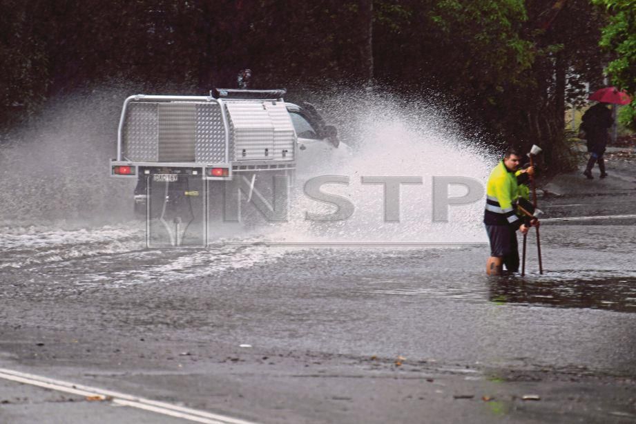 SEORANG pekerja membersihkan saluran air yang tersumbat ketika sebuah kenderaan melintasi jalan Railway Terrace di Lewisham, Sydney yang banjir. - EPA