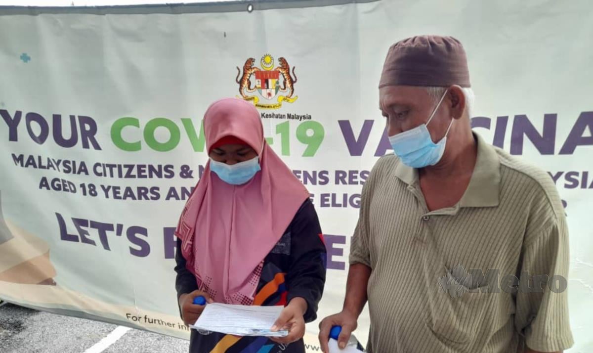 Siti Rosnani dan Rusly meneliti dokumen vaksin selepas menerima suntikan di Kompleks Sukan Masjid Tanah hari ini. FOTO HASSAN OMAR