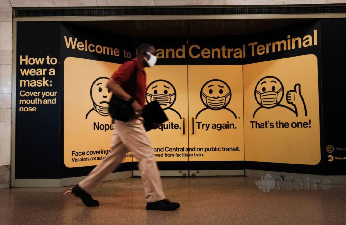 Lelaki berjalan di hadapan iklan pemakaian pelitup muka yang betul di Grand Central Terminal, New York. FOTO AFP.