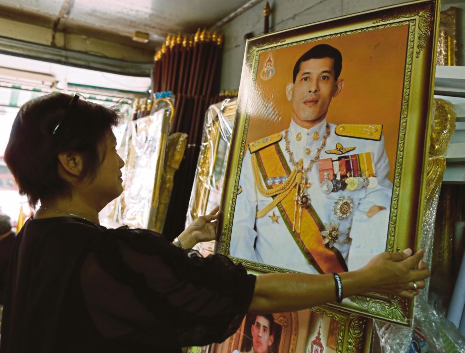 SEORANG wanita menggantung gambar Putera Mahkota Thailand, Maha Vajiralongkorn di kedainya di Bangkok kelmarin. - EPA 