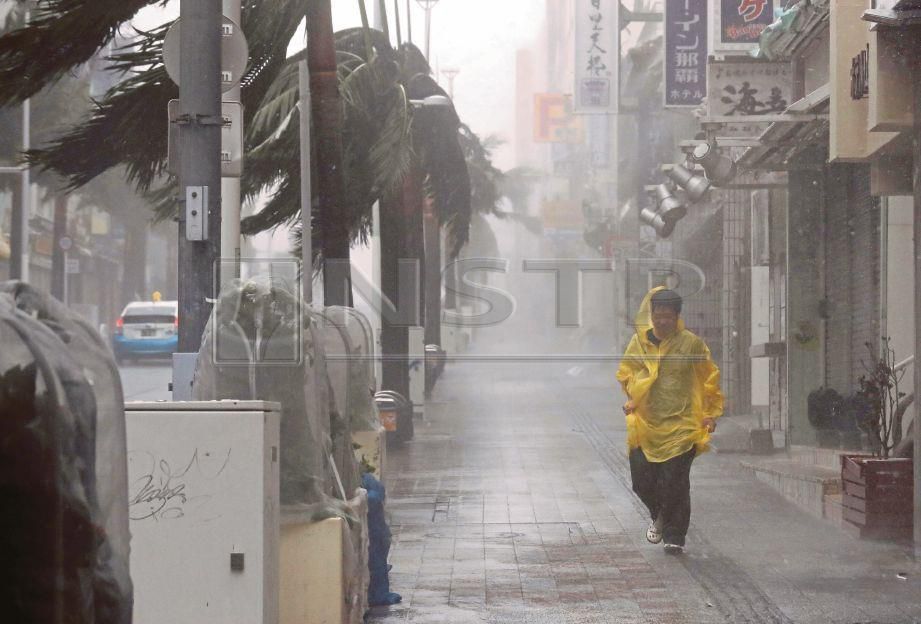 SEORANG lelaki berjalan  dalam hujan lebat dan angin kencang yang disebabkan oleh Taufan Trami di  Naha,  Okinawa. - Reuters