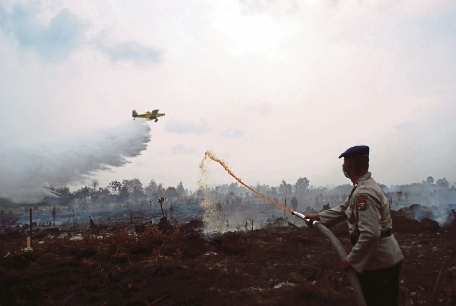  SEBUAH pesawat menggugurkan  air sementara  seorang anggota polis menyembur air untuk memadamkan kebakaran tanah gambut di Kampar, Riau, kelmarin. - Antara
