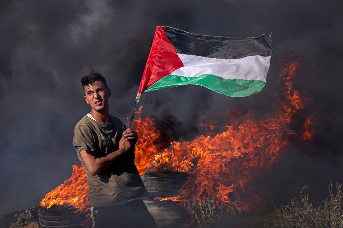 PEMUDA Palestin di timur Gaza memegang bendera sambil berdiri di hadapan tayar yang terbakar sebagai protes terhadap serangan Israel di Tebing Barat. FOTO AFP.