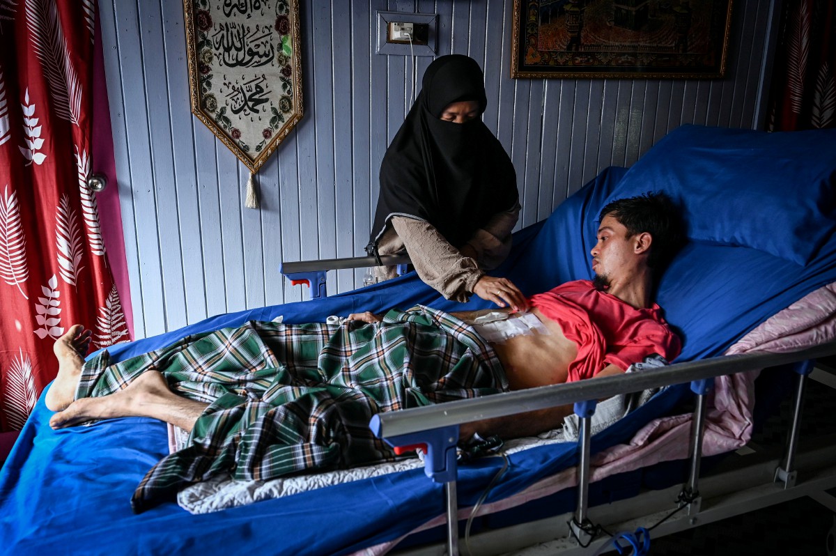 ZALIHA (kiri) menguruskan anaknya, Abdul Mukmin yang terlantar ketika ditemui di Kampung Kuala Tepuh hari ini. FOTO Bernama 