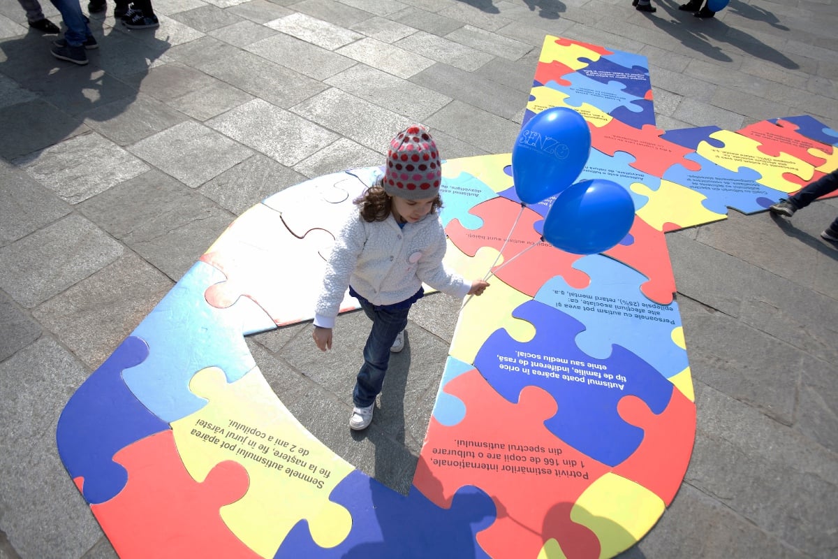 A child holding blue baloons walks over the sign of Autism Awarness in Bucharest city April 2, 2014. International Autism Awareness Day was marked by a march downtown Bucharest and the blue lighting up of several important institutional buildings in Bucharest. AFP PHOTO / MIRCEA RESTEA (Photo by MIRCEA RESTEA / AFP)