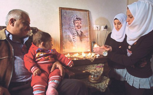 SEBUAH keluarga menyalakan lilin di depan portret Yasser bagi memperingati tarikh kematiannya, hari ini.