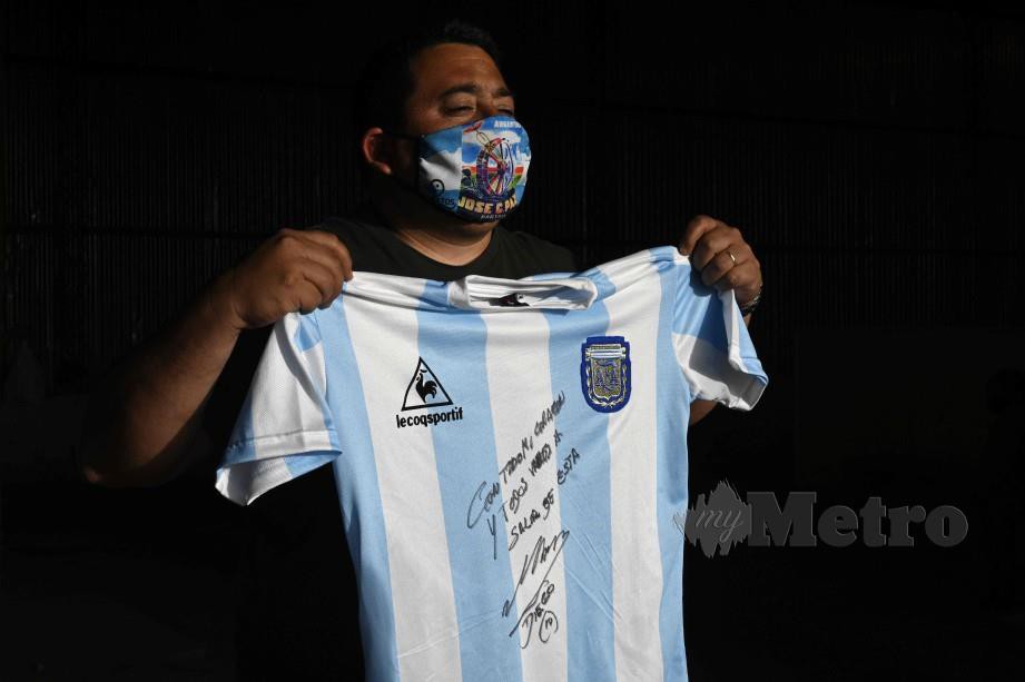 SEORANG penduduk memegang jersi yang ditandatangani oleh Maradona. FOTO AFP 