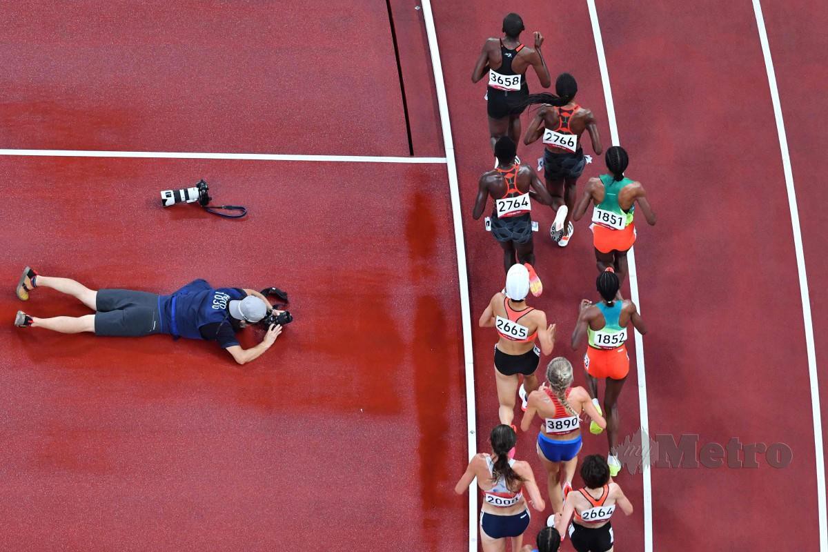 SEORANG jurugambar dilihat mengambil gambar atlet beraksi dalam acara saringan 5000m di Stadium Olimpik Tokyo hari ini. FOTO AFP
