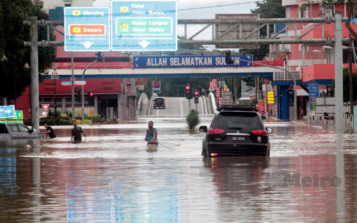ORANG ramai cuba menarik dua kenderaan tersangkut dalam air selepas meredah banjir di Jalan Tun Habab, Kota Tinggi. FOTO ZAIN AHMED