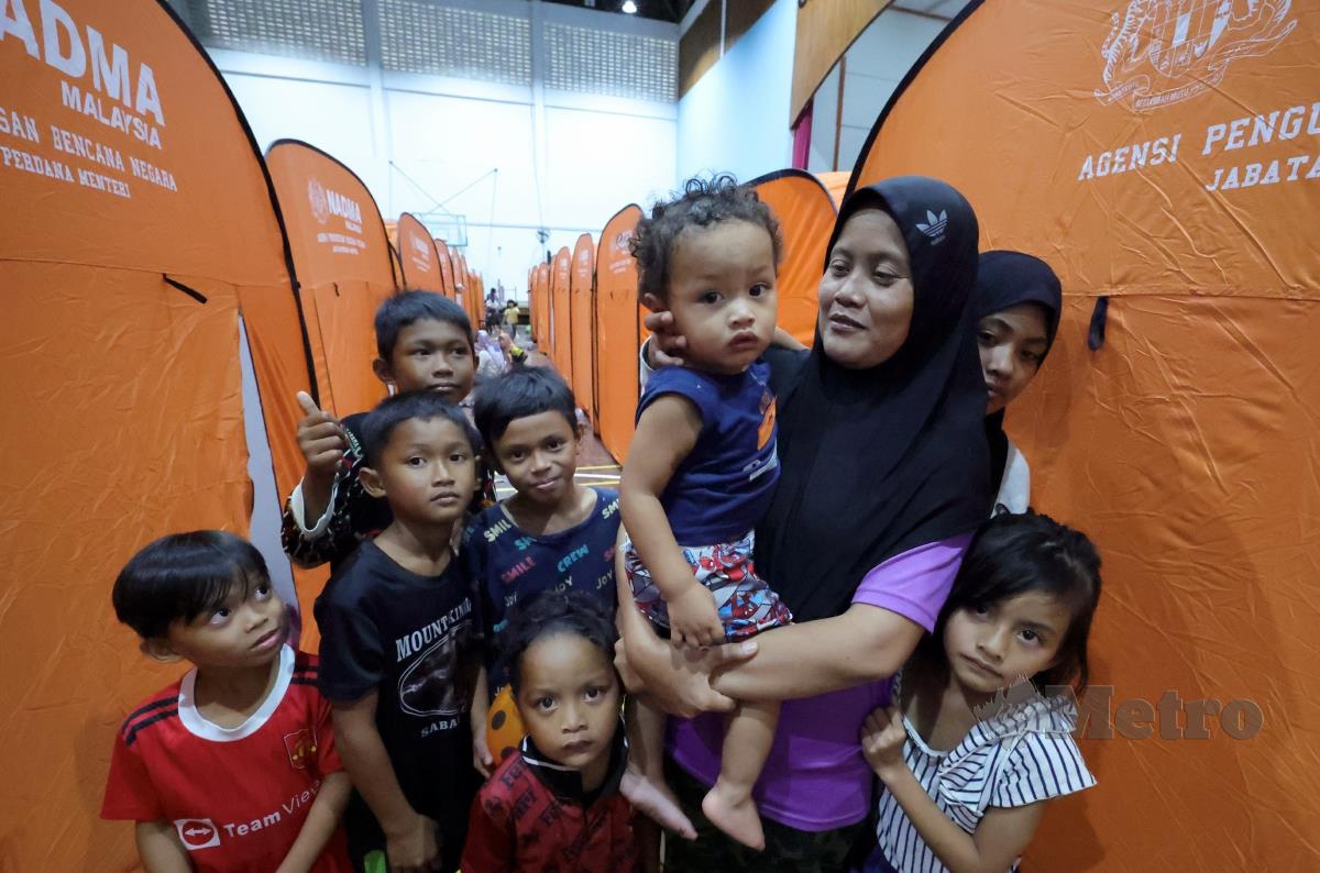 Seorang ibu, Latifah Ayuh  Zainal, 35, mendukung anaknya Zafrul Zubair, berusia setahun, bersama anak-anak saudaranya yang ditempatkan di Pusat Pemindahan Sementara (PPS) Dewan Chong Hua Kota Belud. FOTO BERNAMA