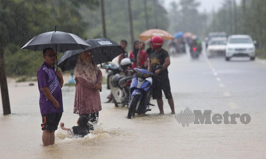 Penduduk meredah banjir dalam keadaan berhujan di Kampung Buloh, Permaisuri. FOTO Ghazali Kori