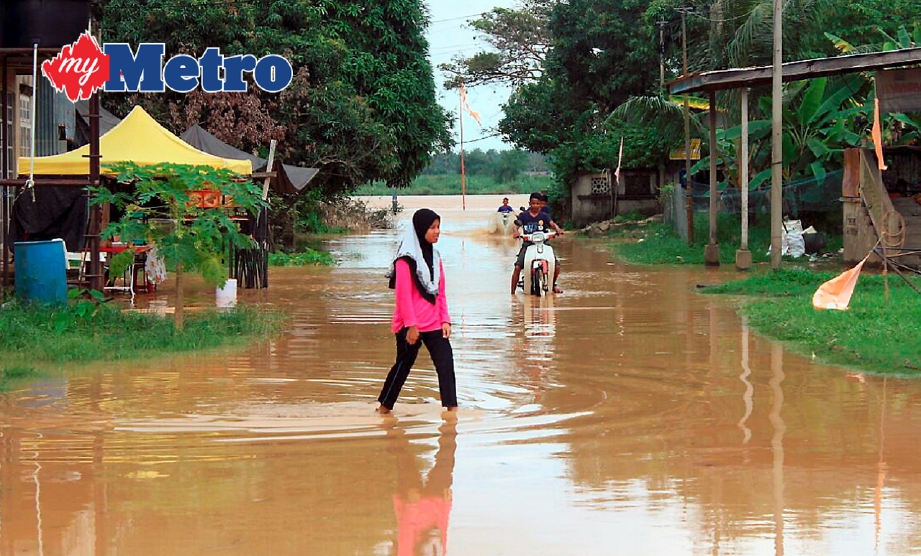 Penduduk mengharungi banjir di hadapan rumah mereka akibat limpahan Sungai Kelantan yang meningkat berdekatan Dataran Purnama di Kampung Laut, Tumpat. FOTO Nik Abdullah Nik Omar