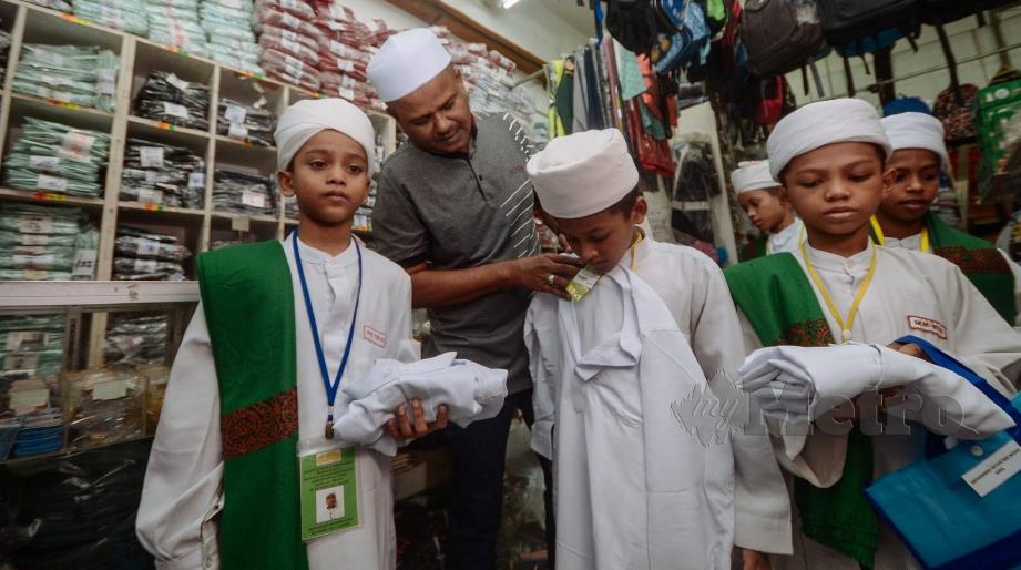 KHADAR Shah (dua dari kiri) membantu pelajar tahfiz memilih pakaian hari raya di Bandar Perda, Bukit Mertajam, semalam. FOTO Shahnaz Fazlie Shahrizal.