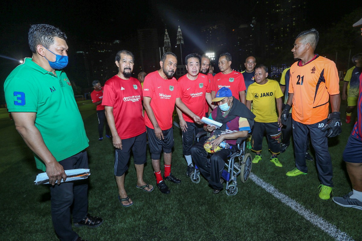 Bekas pemain Selangor dan Kelab Sultan Sulaiman, Kamal Bahrin (berkerusi roda) menerima sumbangan dari Mohd Firdaus (tiga kiri) ketika hadir menyaksikan perlawanan amal bolasepak persahabatan di Kampung Baru.