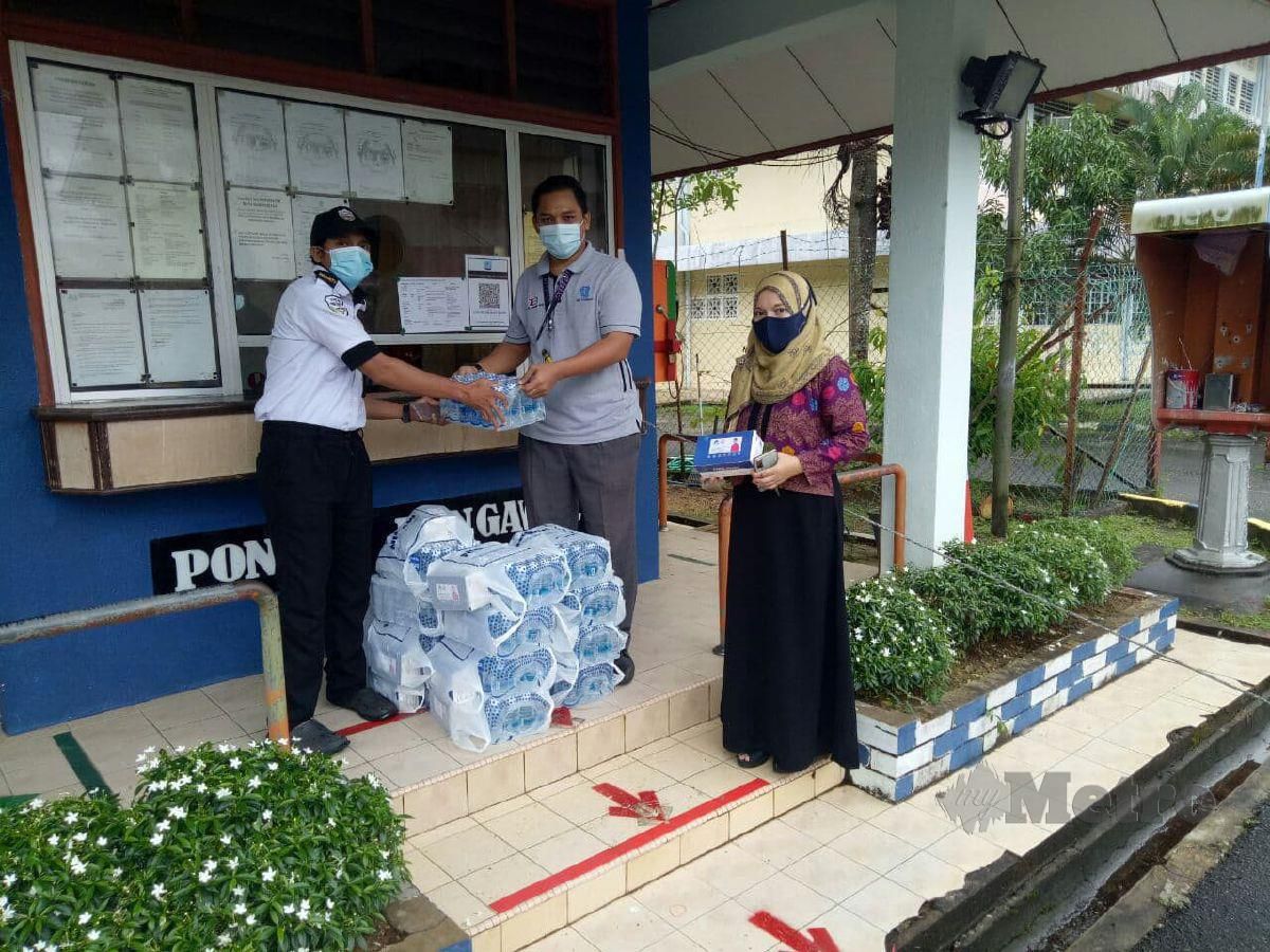 AZWAN Nazzul (dua kanan) menyerahkan air mineral kepada Fairuddin (kiri) disaksikan Norizah untuk kegunaan calon SPM yang menjalani proses kuarantin di asrama SMK Bukit Besar, di sini, hari ini. FOTO Baharom Bakar