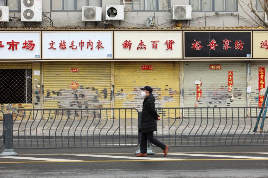 LELAKI memakai penutup mulut dan hidung berjalan di depan deretan kedai yang tidak beroperasi di Wuhan, Hubei. FOTO Reuters