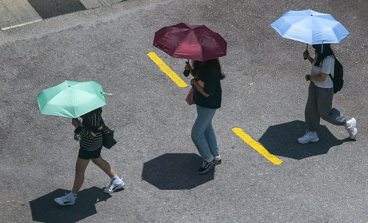 Orang ramai berjalan menggunakan payung untuk berteduh dari cuaca panas terik.
