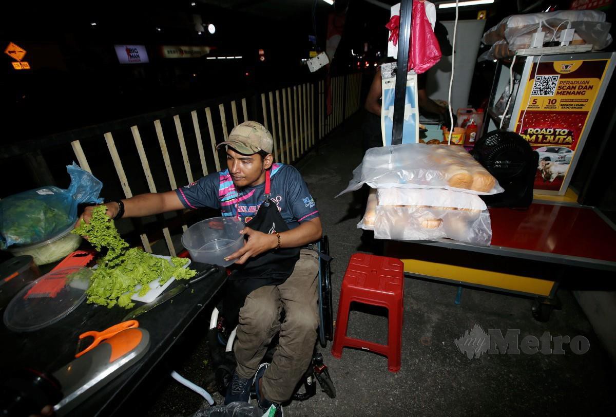MUHAMAD Fakhruddin yang berkerusi roda mencari rezeki dengan menjual burger di Taman Maluri. FOTO Eizairi Shamsudin