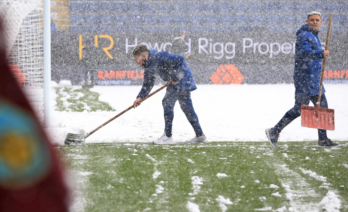 Petugas stadium membersihkan kawasan padang yang dilitupi salji tebal di Turf Moor. FOTO AFP 