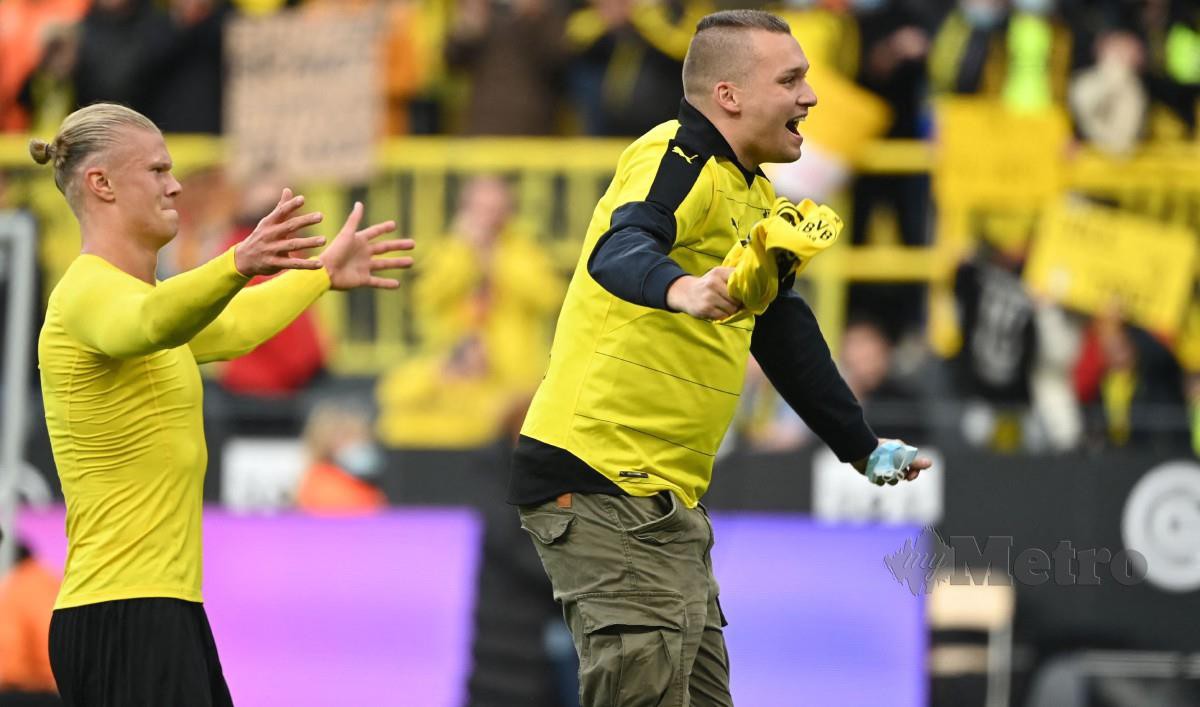 HAALAND (kiri) meraikan kemenangan Dortmund bersama seorang penyokong yang mencerobohi padang. FOTO AFP