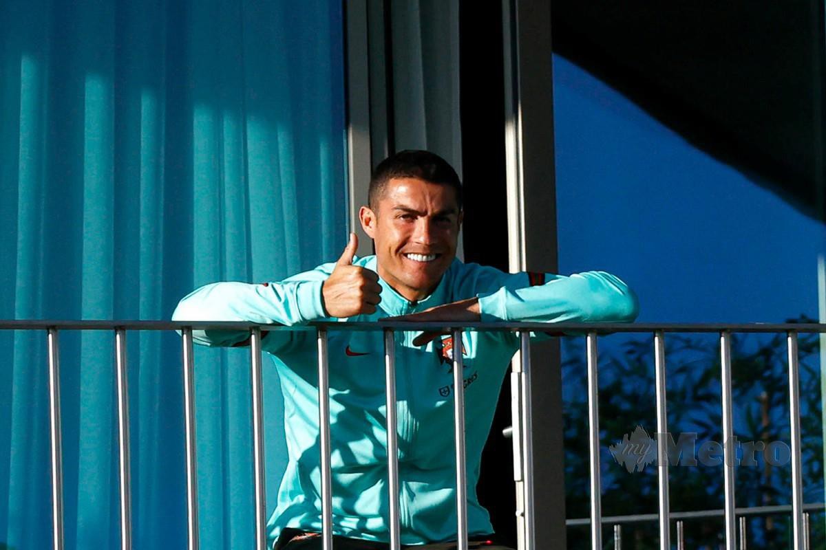 Ronaldo menunjukkan isyarat bagus ketika menyaksikan rakan sepasukan berlatih dari beranda di kem latihan Portugal di Oeiras, Lisbon. FOTO AFP