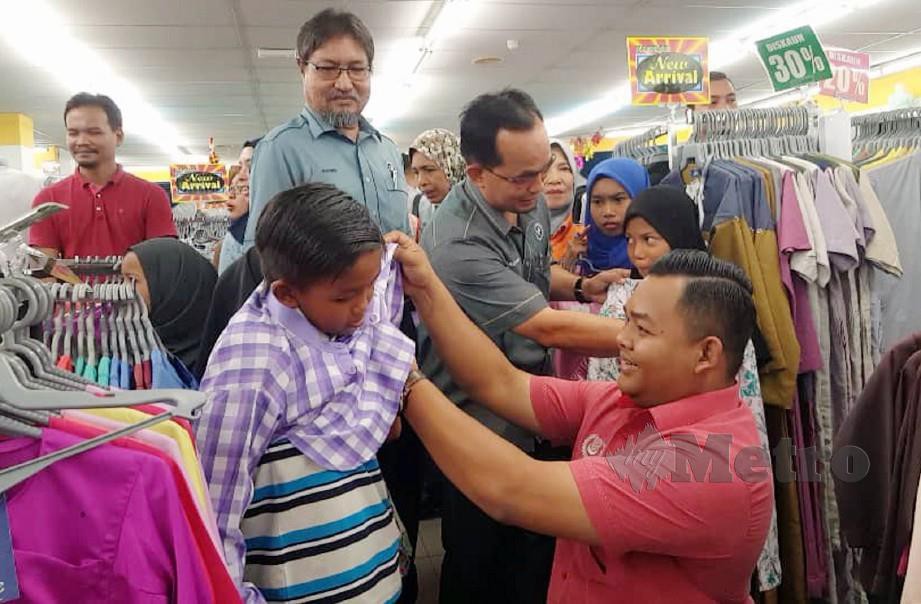 Firdaus (kanan, baju merah) dan Muhd Nasir  (tengah) membantu kanak-kanak mencuba pakaian raya sempena Program Sinaran Kasih di Langkawi.