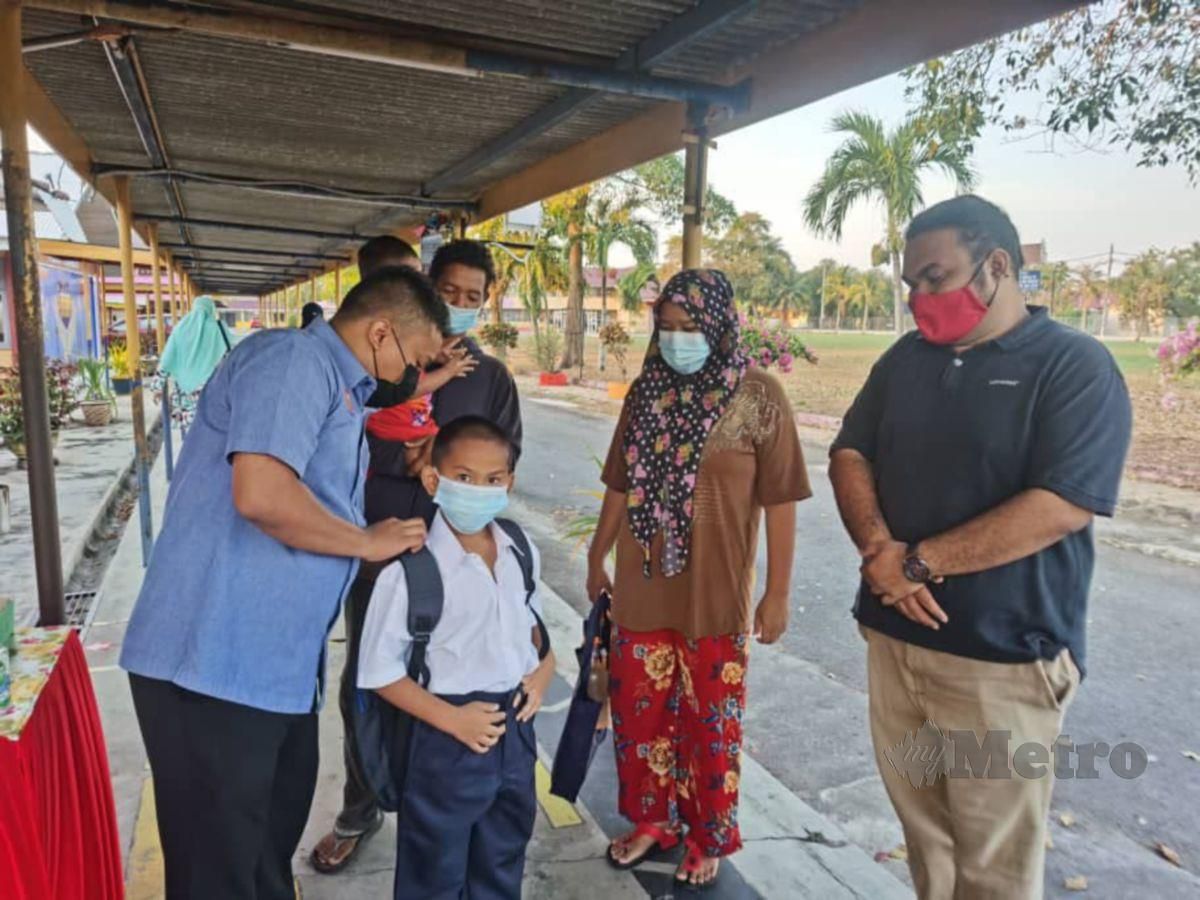 AMIRUL Syahir membantu membetulkan beg sekolah Mohammad Amirul yang mula belajar di SK Telok Kechai, Kuala Kedah ditemani bapanya, Mohd Faizuan dan ibu, Zul Hijah Fadzilah, 31. FOTO ihsan GPMS 