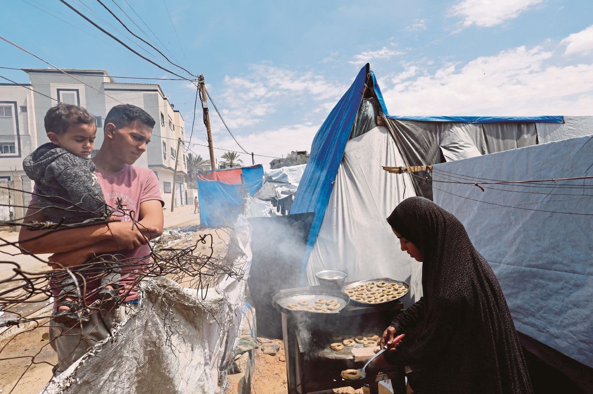 PENDUDUK Palestin yang berlindung di Rafah memasak hidangan Aidilfitri, di luar khemah mereka. FOTO Reuters