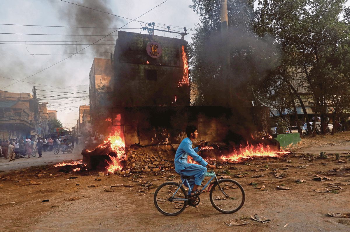 BUDAK lelaki menunggang basikal melepasi pos pemeriksaan yang dibakar penyokong Imran Khan. FOTO Reuters