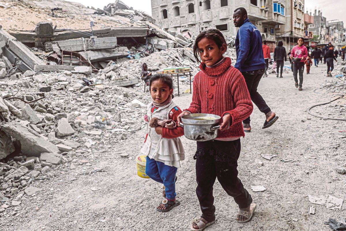 KANAK-KANAK berjalan membawa bekas berisi makanan yang disumbangkan agensi bantuan di kawasan runtuhan bangunan di Rafah. FOTO AFP