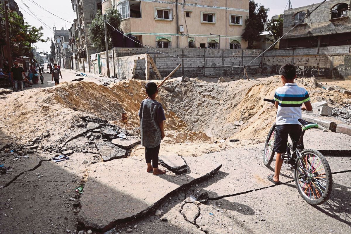 KANAK-KANAK berdiri berhampiran kawah yang disebabkan oleh pengeboman Israel di jalan di Rafah, selatan Gaza. FOTO AFP
