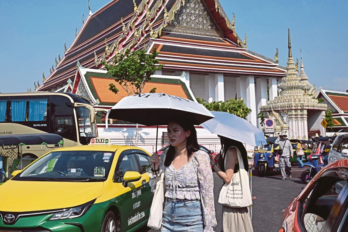 PELANCONG menggunakan payung ketika di luar sebuah tokong di Bangkok. FOTO AFP
